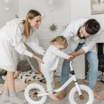 Parents assisting their child with a balance bike in a charming and cozy living room.